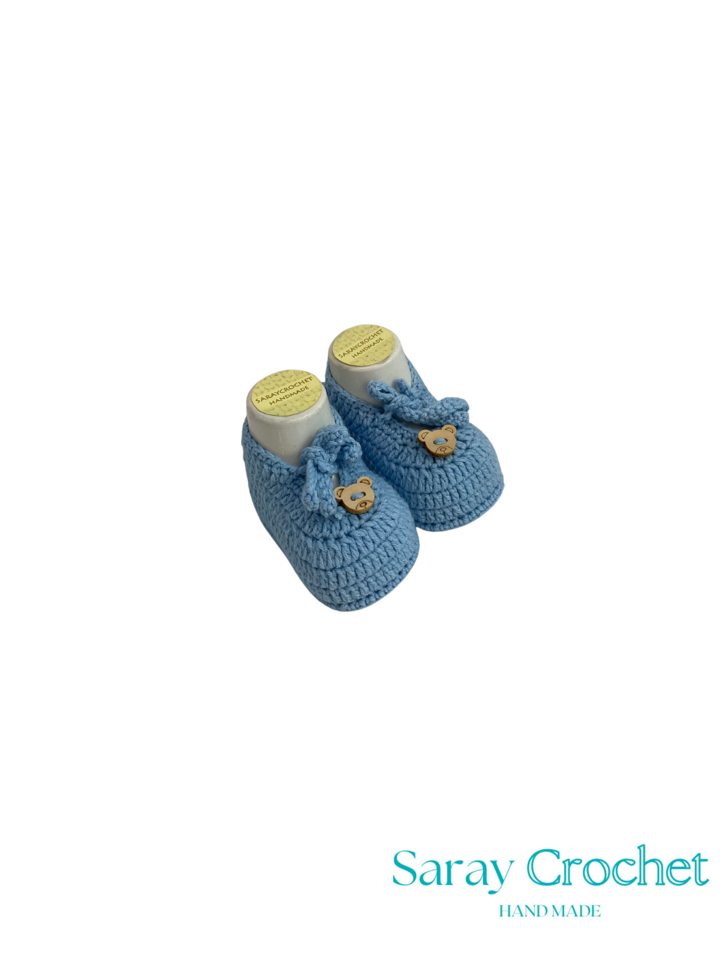 Pair of blue crocheted baby booties with a heart button on a white background, branded 'Saray Crochet'.