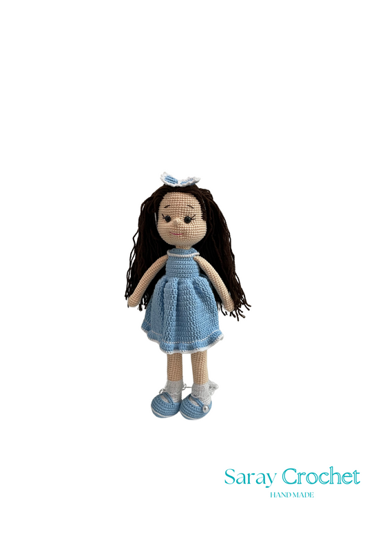 Handmade doll with long brown hair, wearing a blue dress and shoes, standing against a white background with the text 'Saray Crochet'.