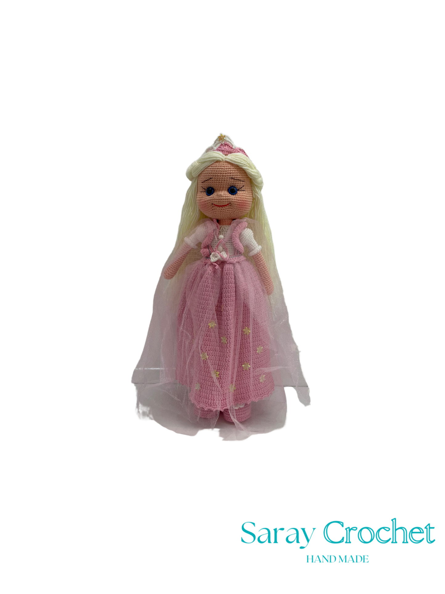 Knitted doll in a pink dress with a white cape on a white background, branded 'Saray Crochet'.