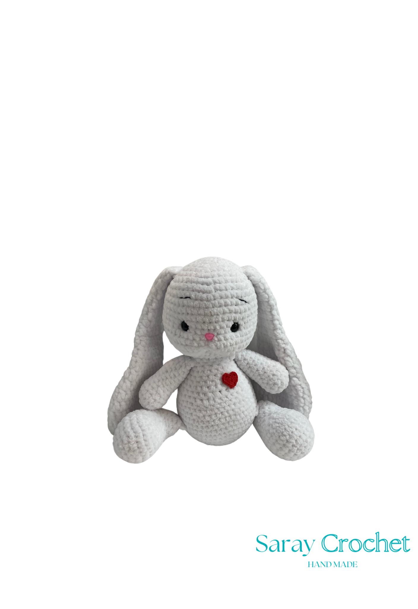 A plush toy rabbit in a sitting position with a pink heart on its chest, long ears, and a smiling face. The toy is made by Saray Crochet and is shown against a white background.