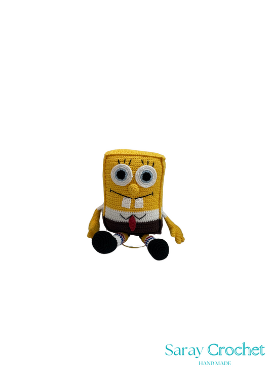Handmade plush toy resembling a cartoon character with a yellow body, a red tie, and a square shape, under the brand name Saray Crochet.