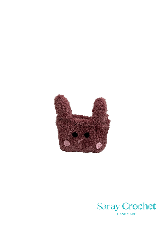 A brown crochet bag with a flat base and rounded top, resembling a animal face with ears, and the brand name 'Saray Crochet' visible.