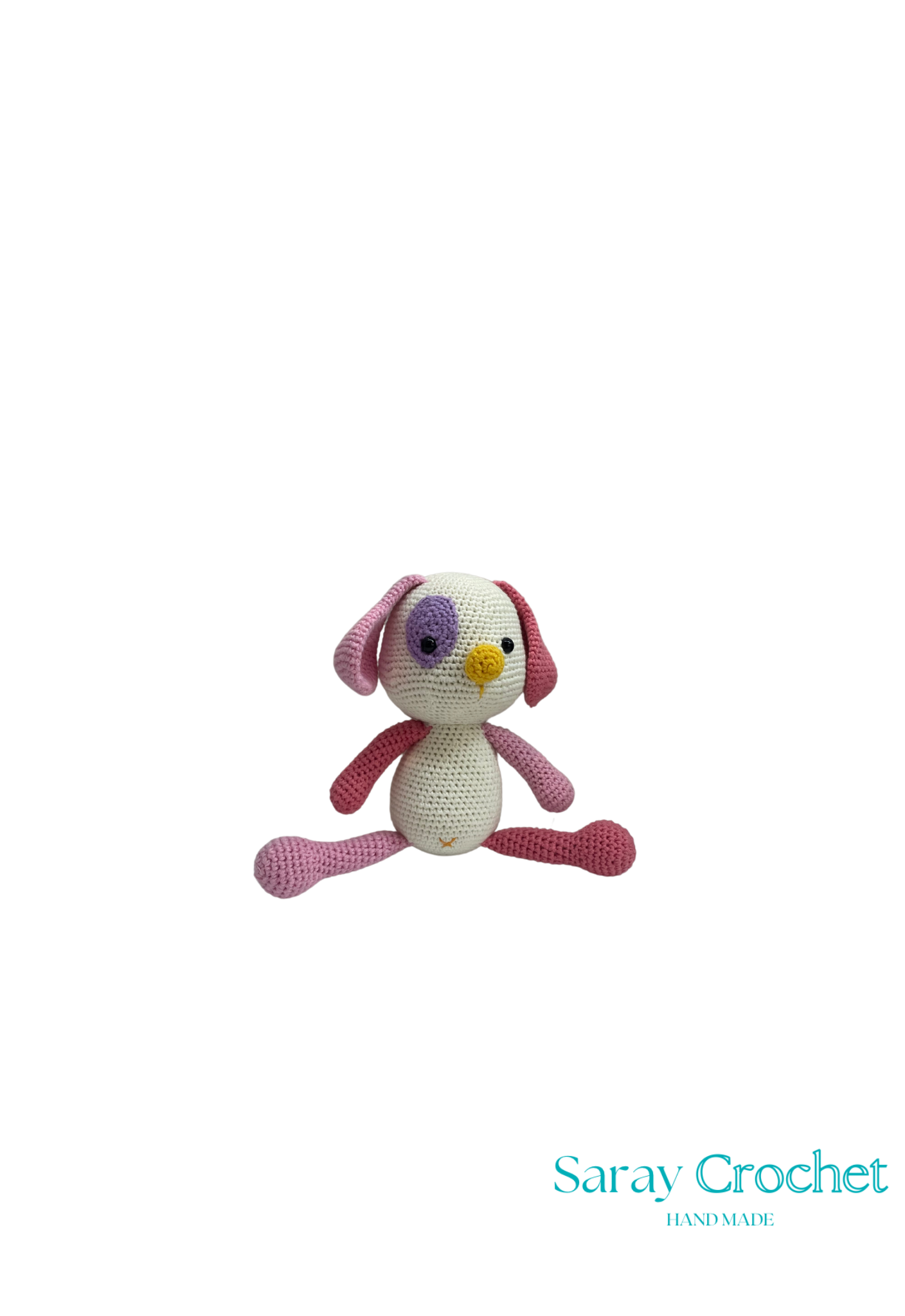 A crochet toy resembling a stylized dog with a pink body, white face, and purple eyes, with the brand name 'Saray Crochet' visible.