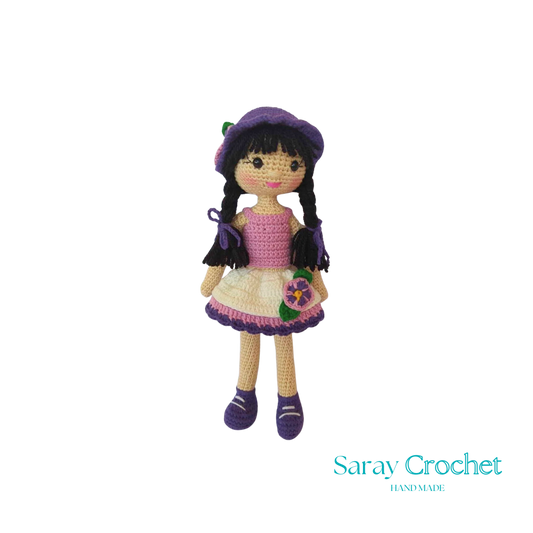 Handmade crochet doll with a pink dress, white details, and a purple hat.