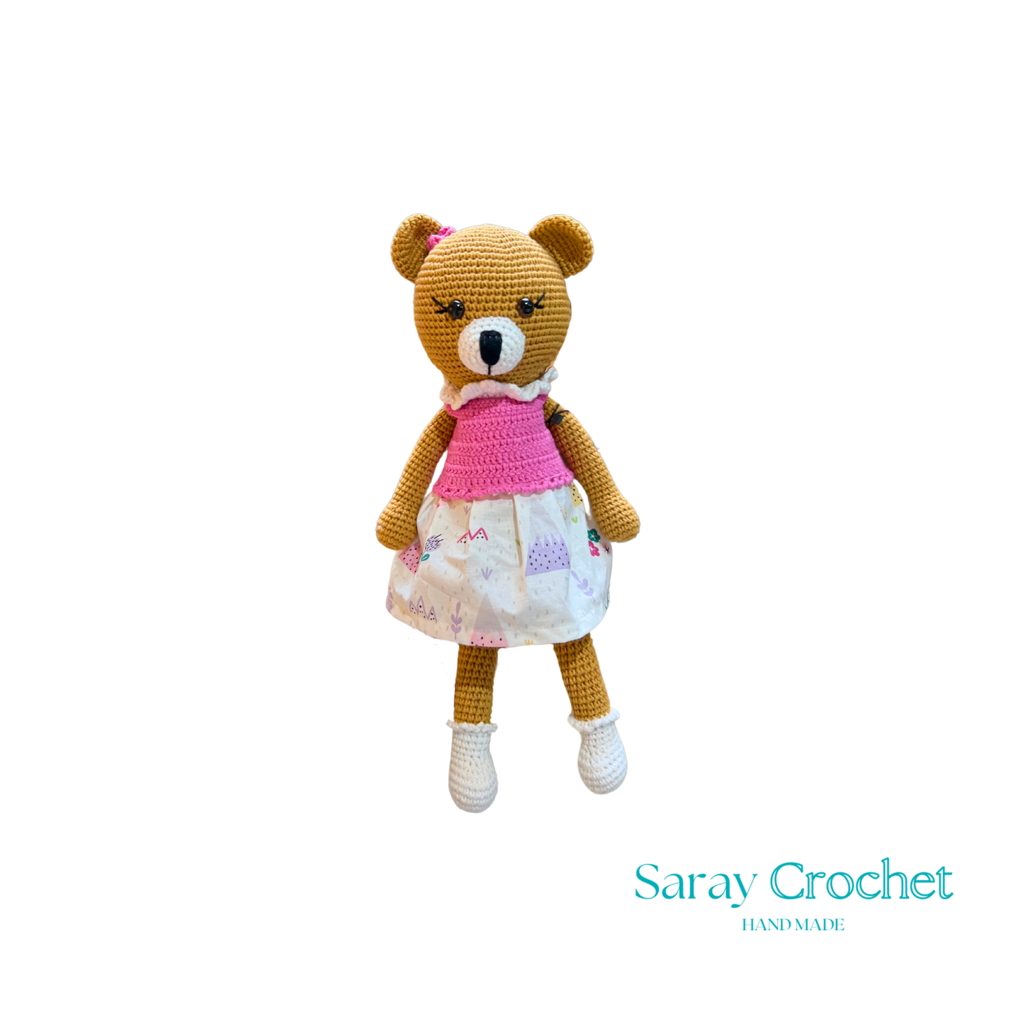Handmade plush toy resembling a bear with a pink dress and white shoes, with the brand name 'SarayCrochet' visible.