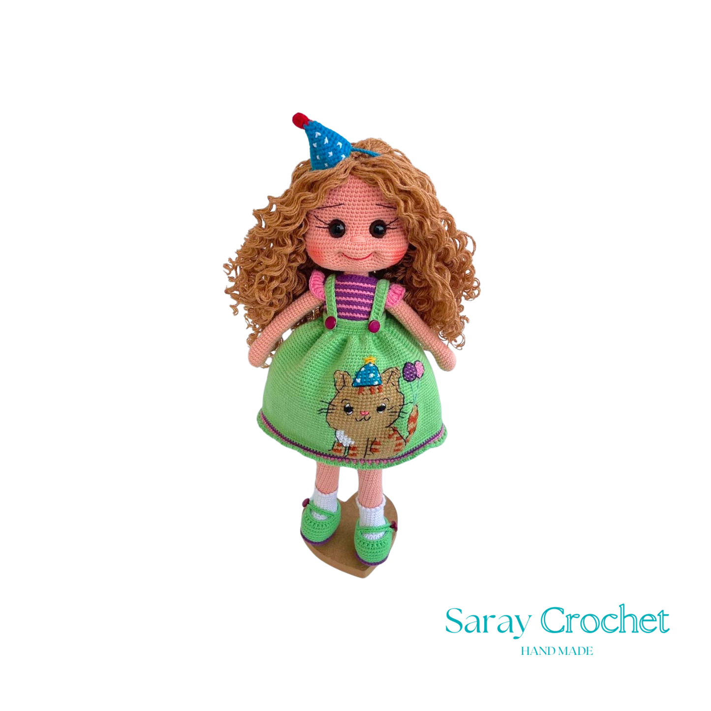 A handcrafted doll with curly orange hair, wearing a green dress with a bear motif and a birthday cap, and green shoes.