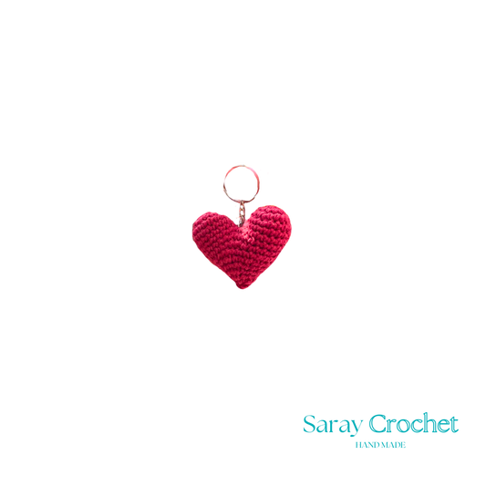 A red heart-shaped pendant with a design resembling a face, possibly a stylized representation of a person or an abstract design.