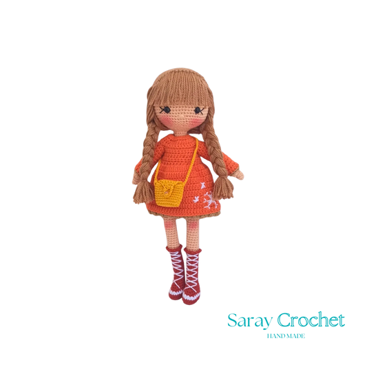 Handmade crocheted doll with orange winter coat and scarf, beige boots, and brown hair.