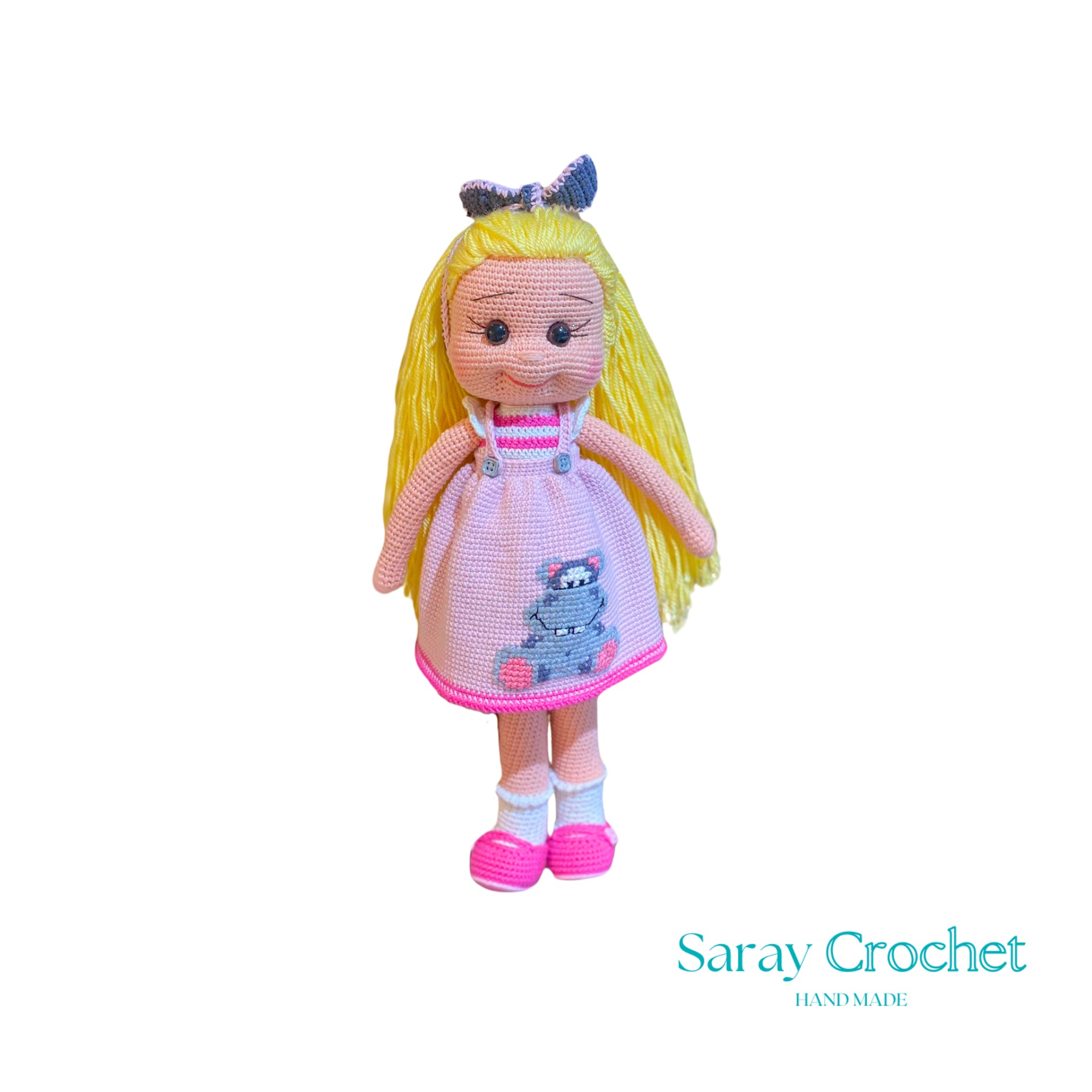 Handmade crochet doll with blonde hair, wearing a pink dress and white and pink shoes, standing against a black background.