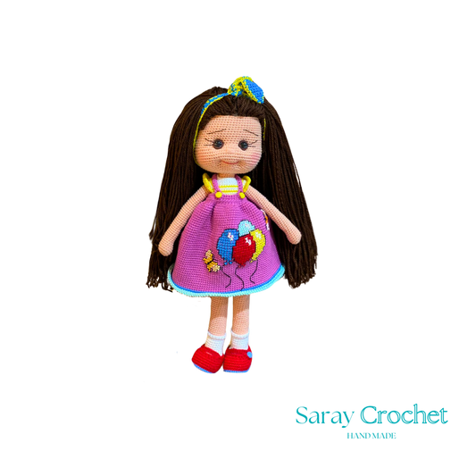 Handmade doll with long brown hair, wearing a purple dress with balloon print and red shoes, with a blue bow in her hair.
