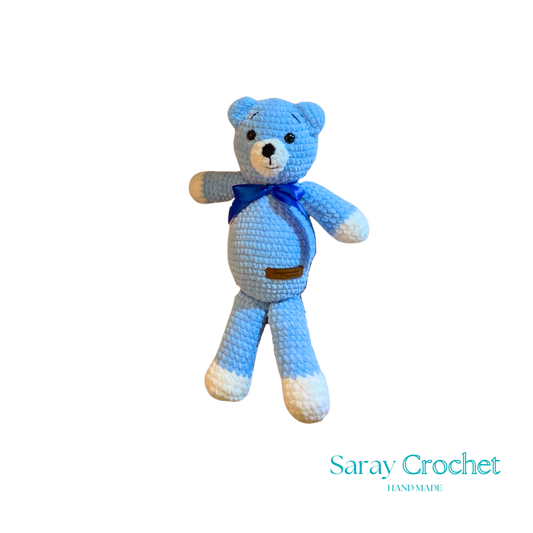 Blue crocheted teddy bear with a blue bow tie on a white background, branded 'Saray Crochet'.