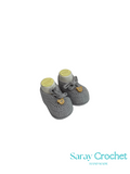 Pair of gray crochet baby booties with yellow accents on a white background, branded 'Saray Crochet'.