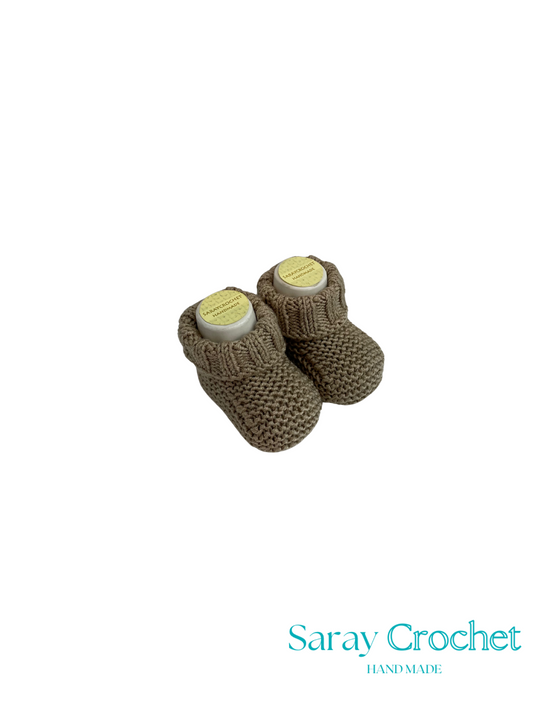 Pair of brown knitted baby booties with labels on a white background, featuring the brand 'Saray Crochet'.