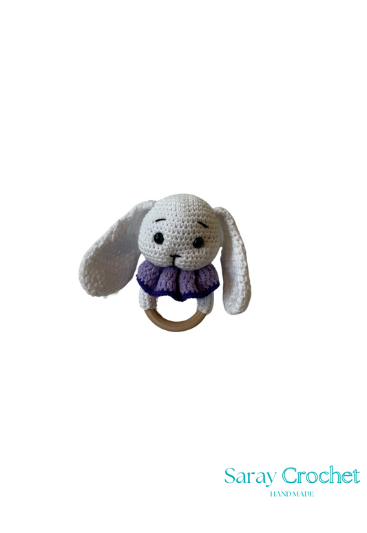 Crocheted bunny rattle with a wooden ring on a white background, branded 'Saray Crochet'.