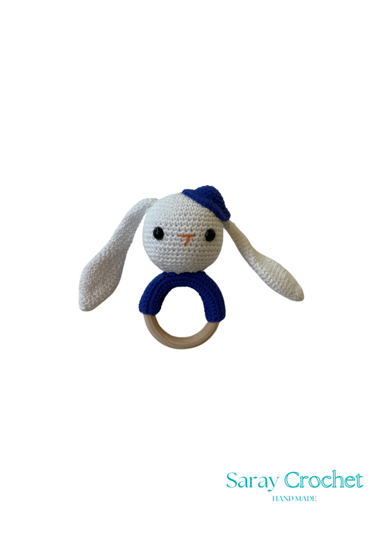 Crocheted bunny rattle with blue hat on a white background, branded 'Saray Crochet'.