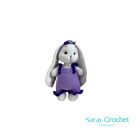 Crocheted bunny toy with purple dress on white background