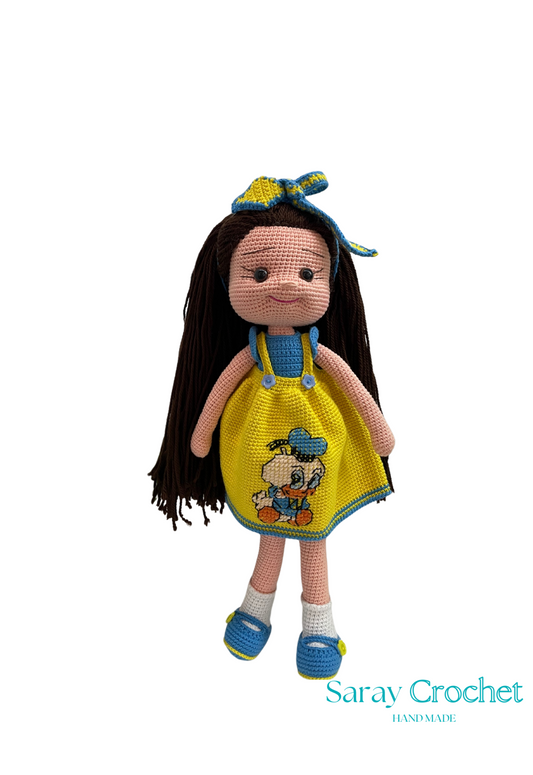Handmade doll with a golden-yellow dress featuring a character, long black hair, and a blue bow on its head.