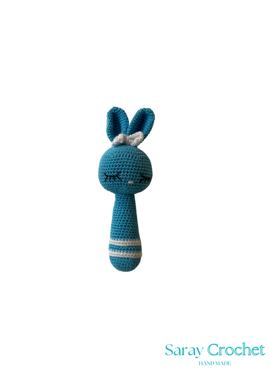A blue and multicolor crochet rattle in the shape of a rabbit with a striped body and a small attached rattle at the bottom.