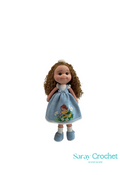 Handmade doll with a blue dress featuring a baby holding a white flower motif, and a white sash in its curly hair.