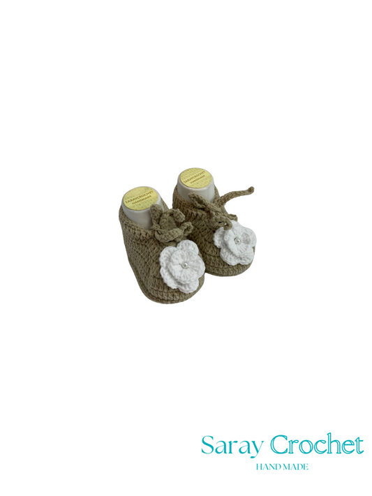 Pair of crocheted baby booties with white flowers on a white background, branded 'Saray Crochet'.