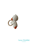 A crochet duck rattle with a beige body, orange beak and feet, and a gray ring attached to its head.