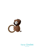 A crochet toy in the shape of a brown monkey sitting on a yellow ring, with the brand name 'Saray Crochet' written at the bottom.