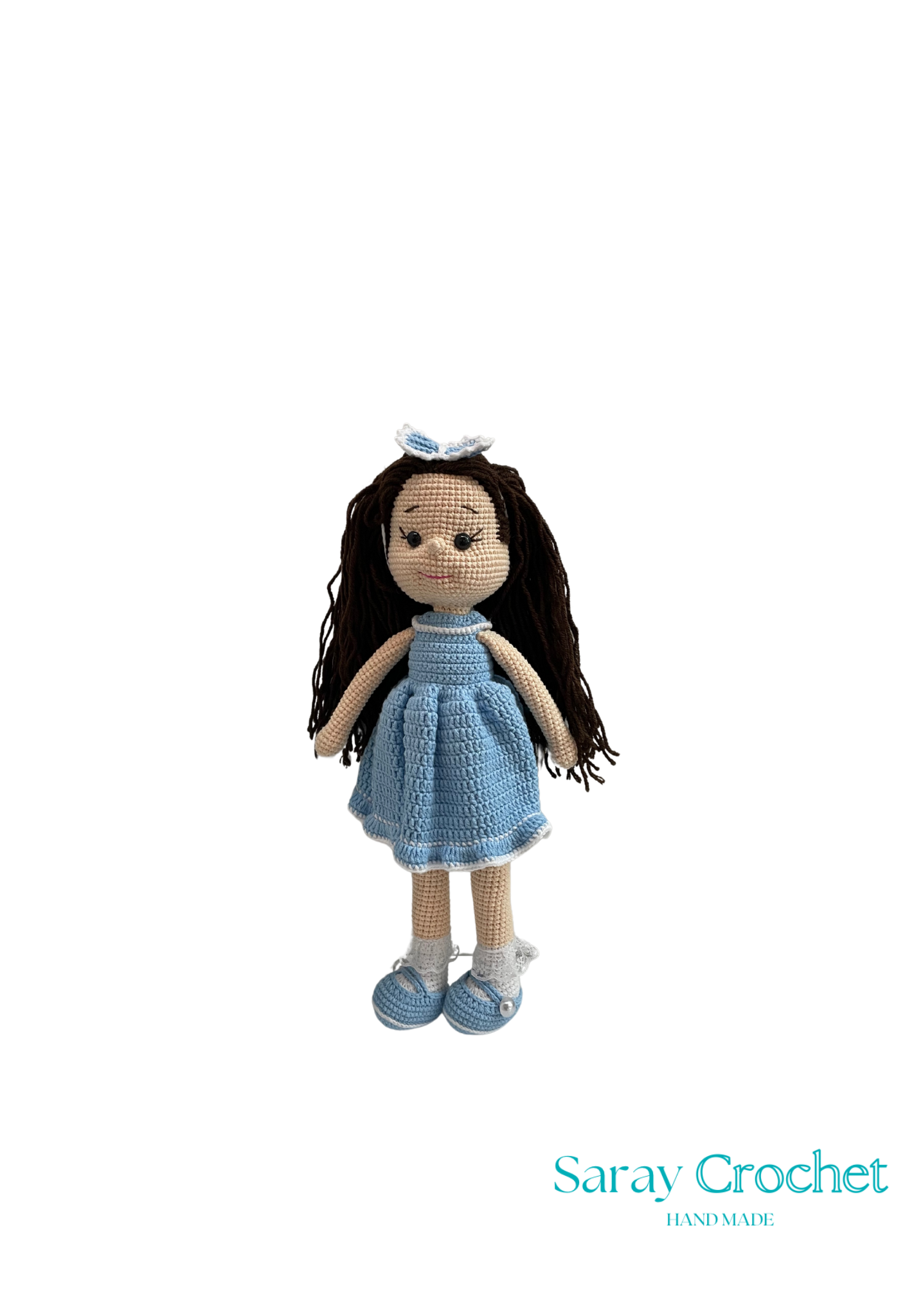 Handmade doll with long brown hair, wearing a blue dress and shoes, standing against a white background with the text 'Saray Crochet'.