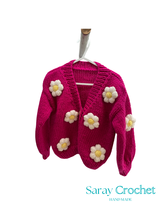Pink crochet cardigan with white flowers on a hanger, branded 'Saray Crochet'.