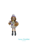 Handmade crochet doll with a white and purple outfit, a hat, and a small bag, standing against a plain background.