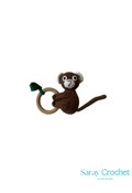 A crochet toy in the shape of a brown monkey with a green tail, hanging from a ring.
