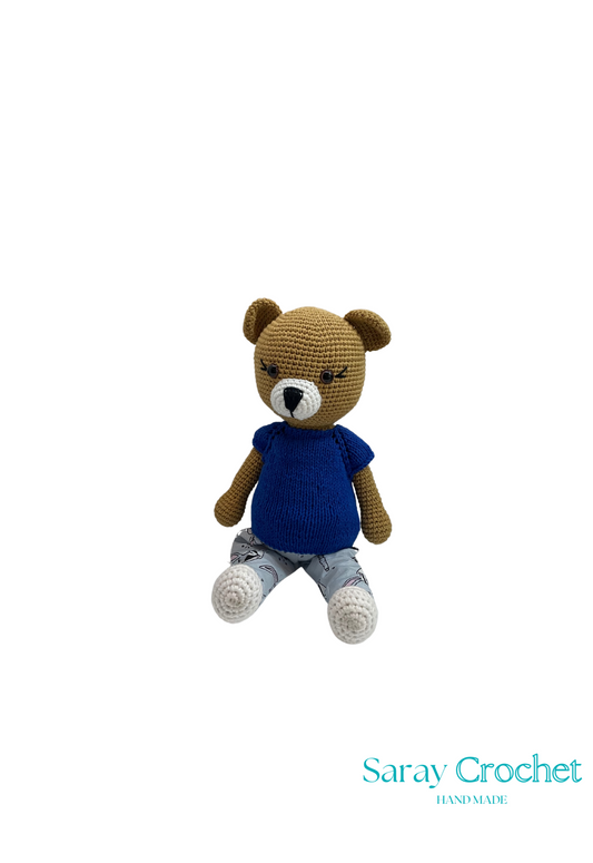 Handmade plush toy resembling a bear with a blue shirt and beige overalls with a zebra pattern, sitting upright.