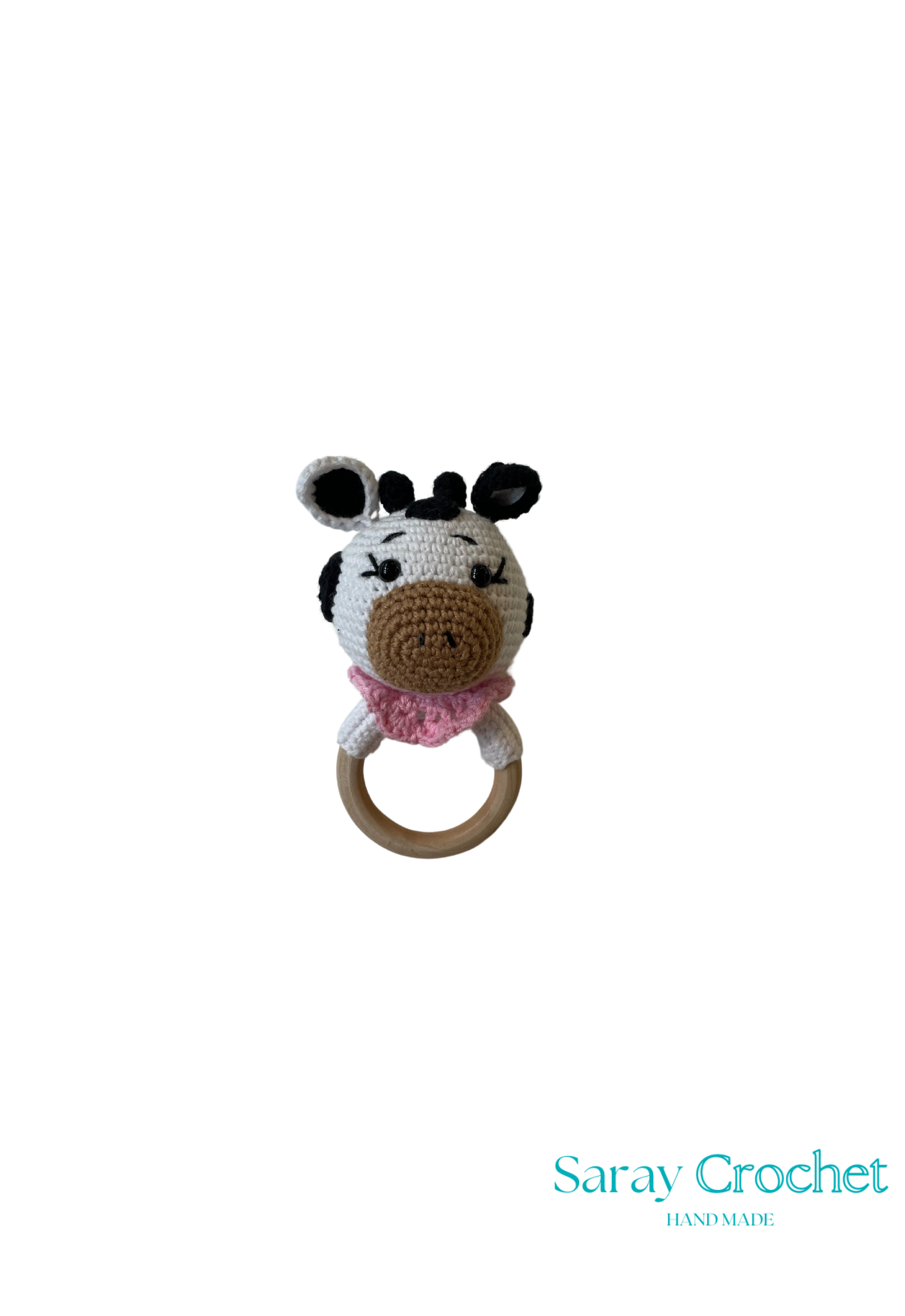 A crochet teething ring toy designed to look like a cow with a predominantly white body and black and brown details, attached to a wooden ring.