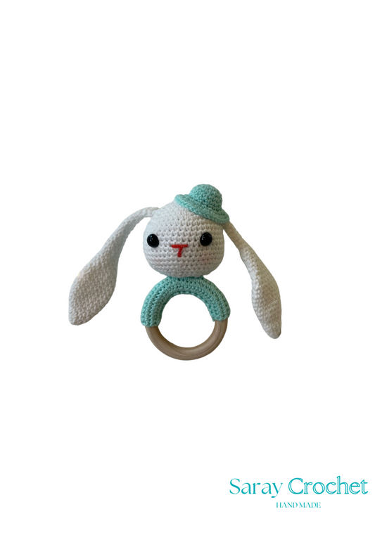 A crochet toy in the shape of a rabbit with a green hat and a ring attached to its head.