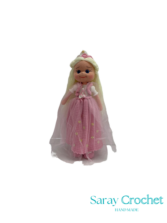 Knitted doll in a pink dress with a white cape on a white background, branded 'Saray Crochet'.