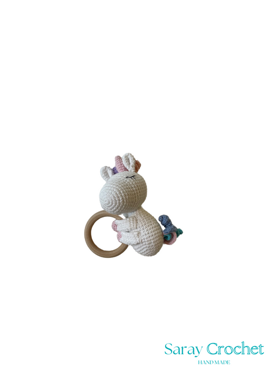 A crochet depiction of a multicolored unicorn, likely a toy or decorative item, with a ring for hanging and a predominantly beige body.