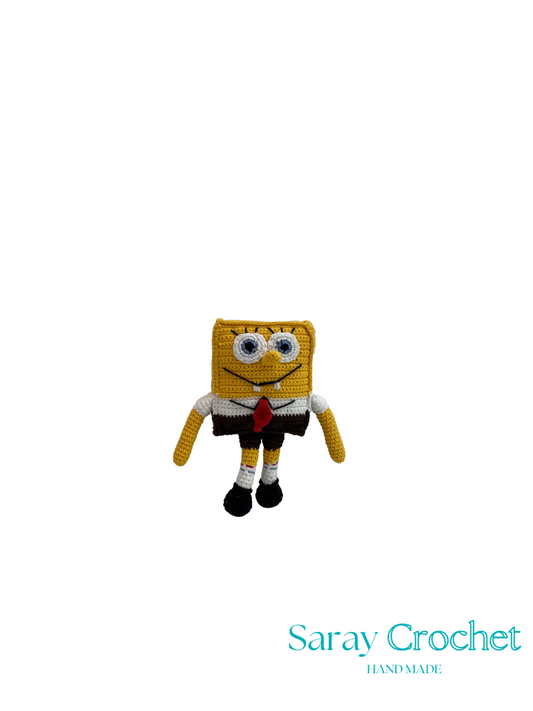 Crocheted plush toy resembling a character with a yellow square head, black shoes, and a red tie on a white background. Brand 'Saray Crochet' is visible.