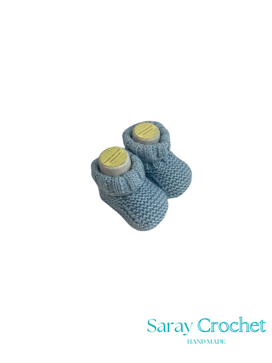 Pair of blue knitted baby booties with yellow labels on a white background, branded 'Saray Crochet'.