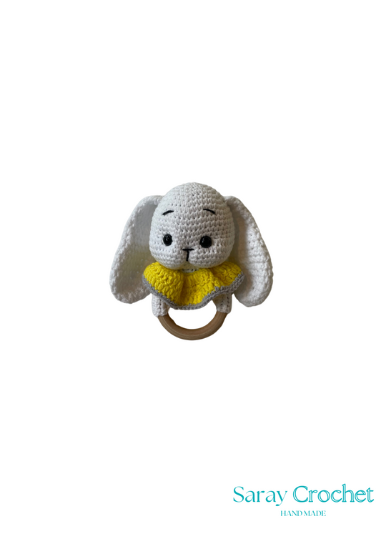 A crochet toy resembling a zvečka (a type of Czech traditional doll) with a gray body and yellow accents, featuring a ring for hanging.