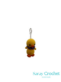 Yellow crocheted duck keychain with a purple scarf on a white background, branded 'Saray Crochet'.
