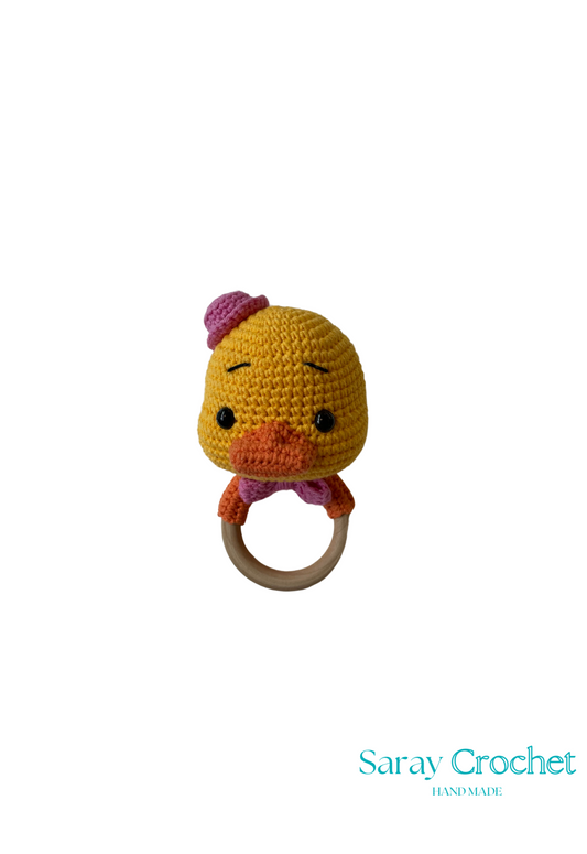 A crochet rattle toy in the shape of a yellow and pink chicken with a wooden ring attached.