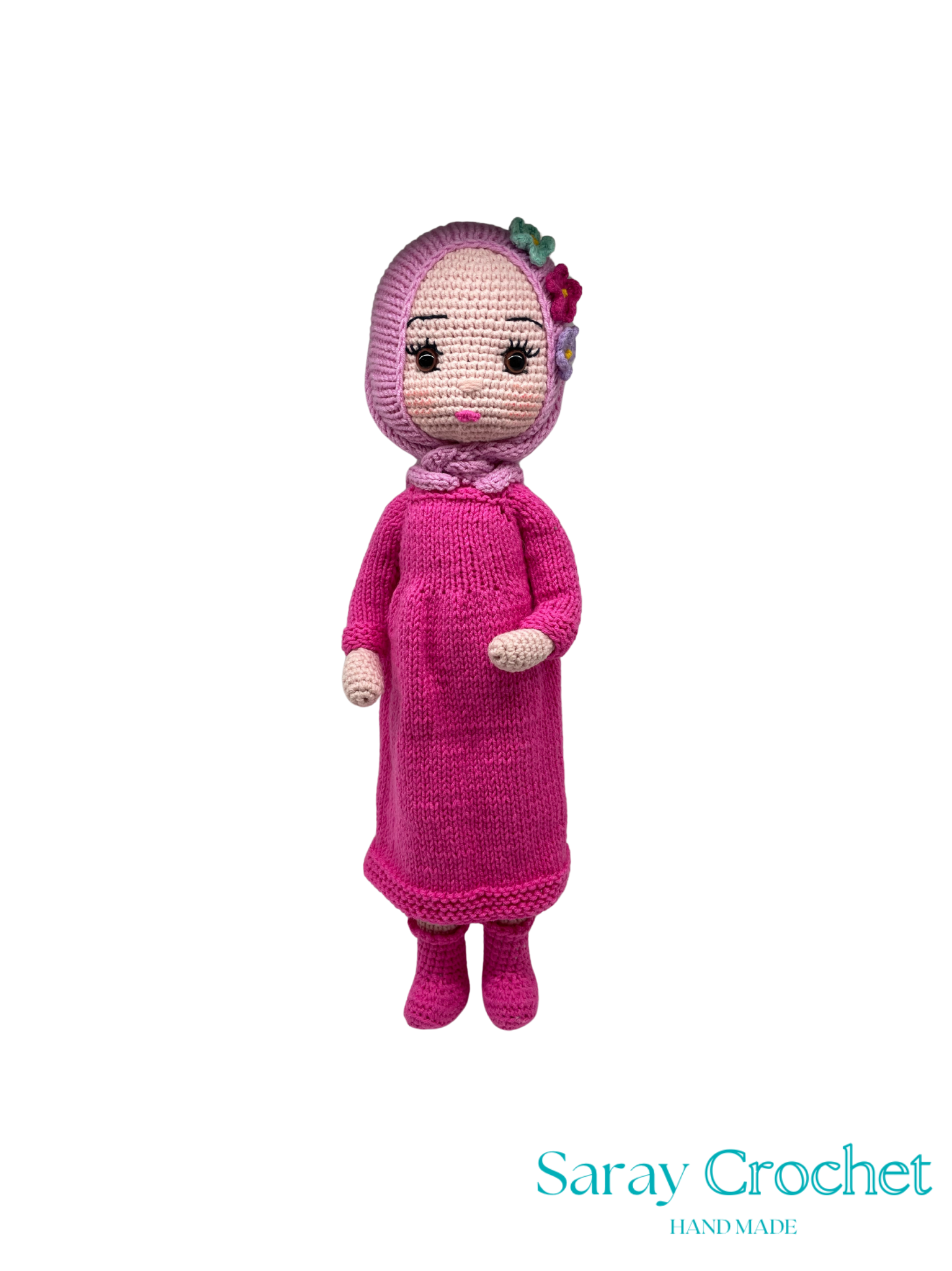 Knitted doll in pink dress with a flower on a white background, branded 'Saray Crochet'.