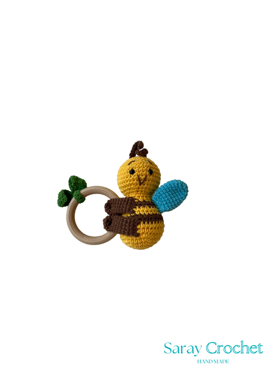 A crochet toy in the shape of a bee with a wooden ring attached, primarily in yellow and blue colors.