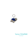 Crocheted dog keychain with blue sweater on a white background, branded 'Saray Crochet'.