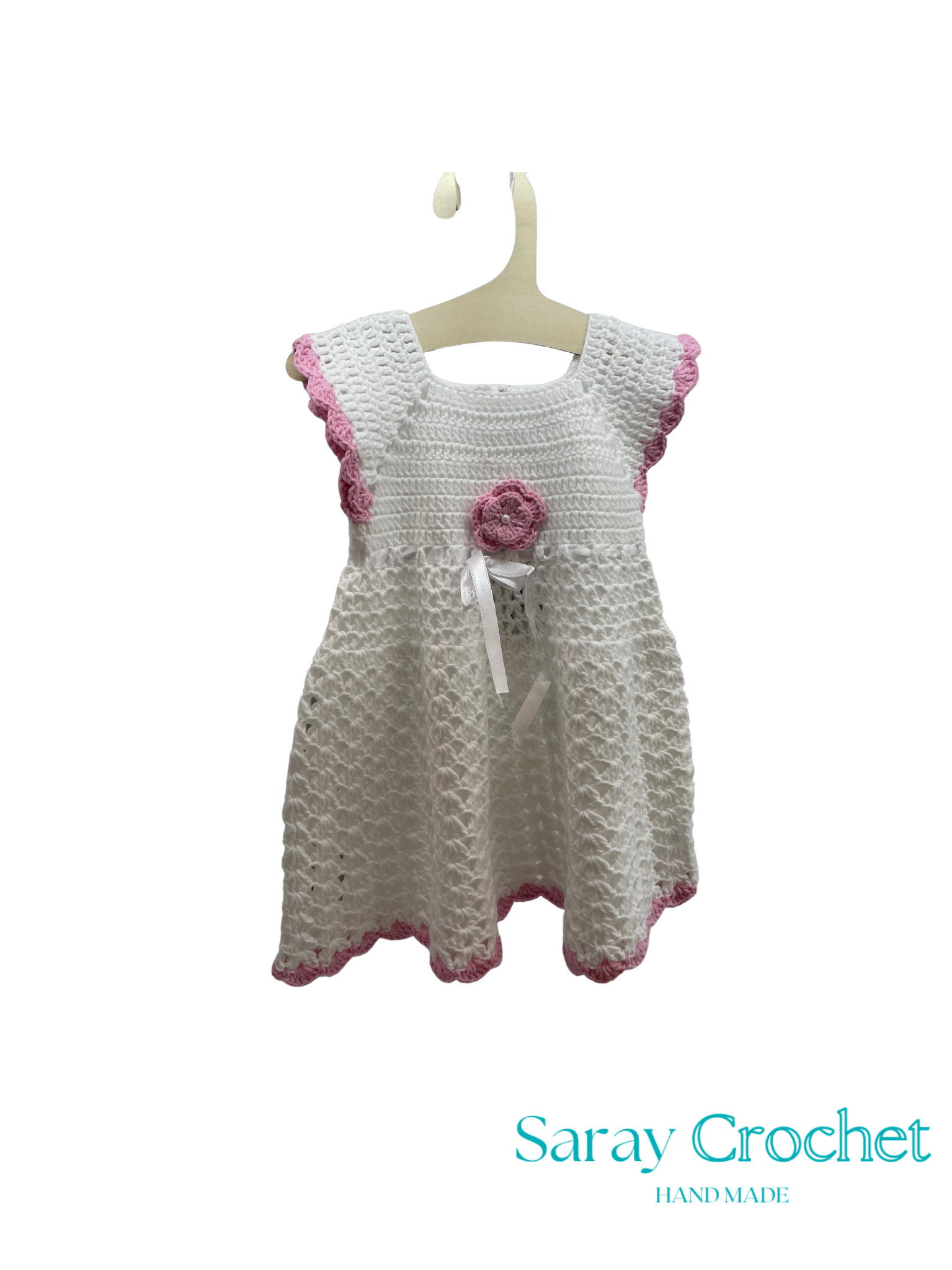 Crocheted dress with pink trim on a hanger, branded 'Saray Crochet'.