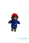 Handmade plush toy resembling Paddington Bear, wearing a blue coat and red hat, standing upright.