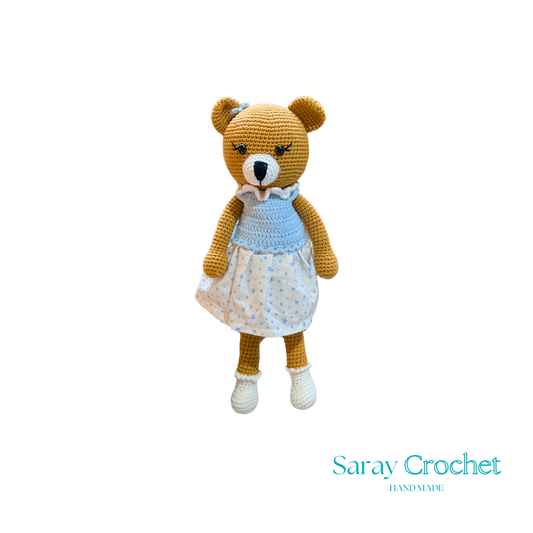 Handmade plush toy resembling a bear with a blue dress and white shoes, on a white background.