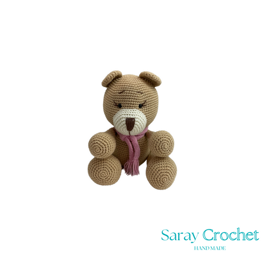 Crocheted teddy bear with a pink scarf on a white background, branded 'Saray Crochet'.