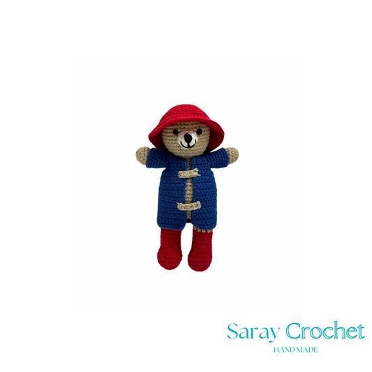 Crocheted teddy bear in a blue coat and red hat on a white background with 'Saray Crochet' branding.