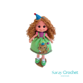 A handcrafted doll with curly orange hair, wearing a green dress with a bear motif and a birthday cap, and green shoes.