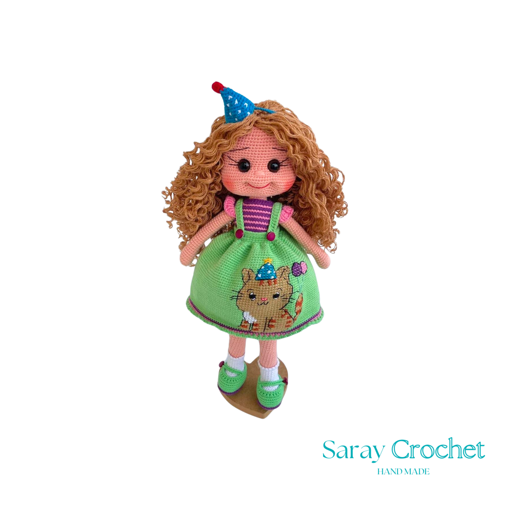 A handcrafted doll with curly orange hair, wearing a green dress with a bear motif and a birthday cap, and green shoes.